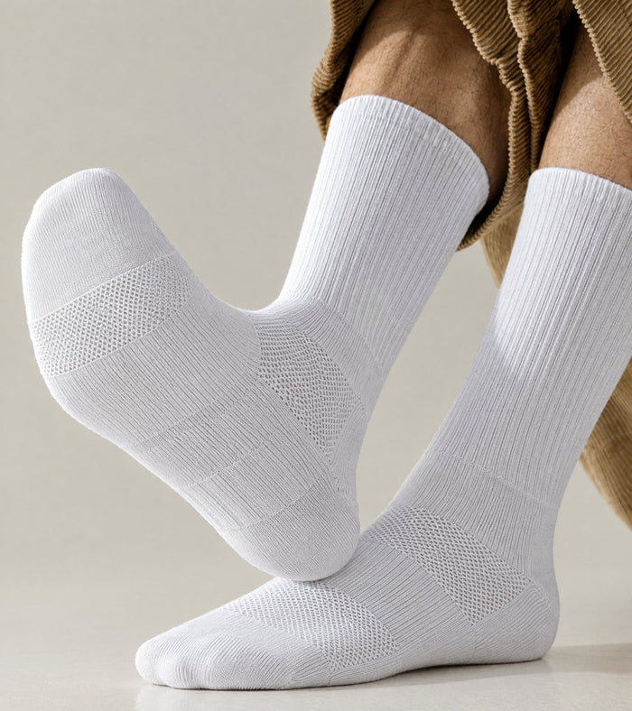 A pair of white crew socks worn on a person's feet, shown against a neutral light beige background with a brown corduroy garment visible at the top.