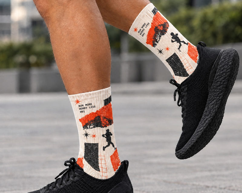 A person outdoors wearing black sneakers and crew socks with a bold orange, black, and off-white graphic print featuring running silhouettes and text.