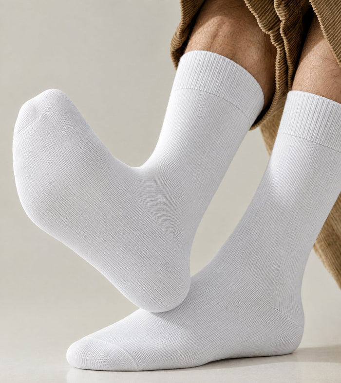 A pair of white crew socks worn on a person's feet, with the lower legs and hem of a brown corduroy trouser leg visible against a clean light beige studio background.