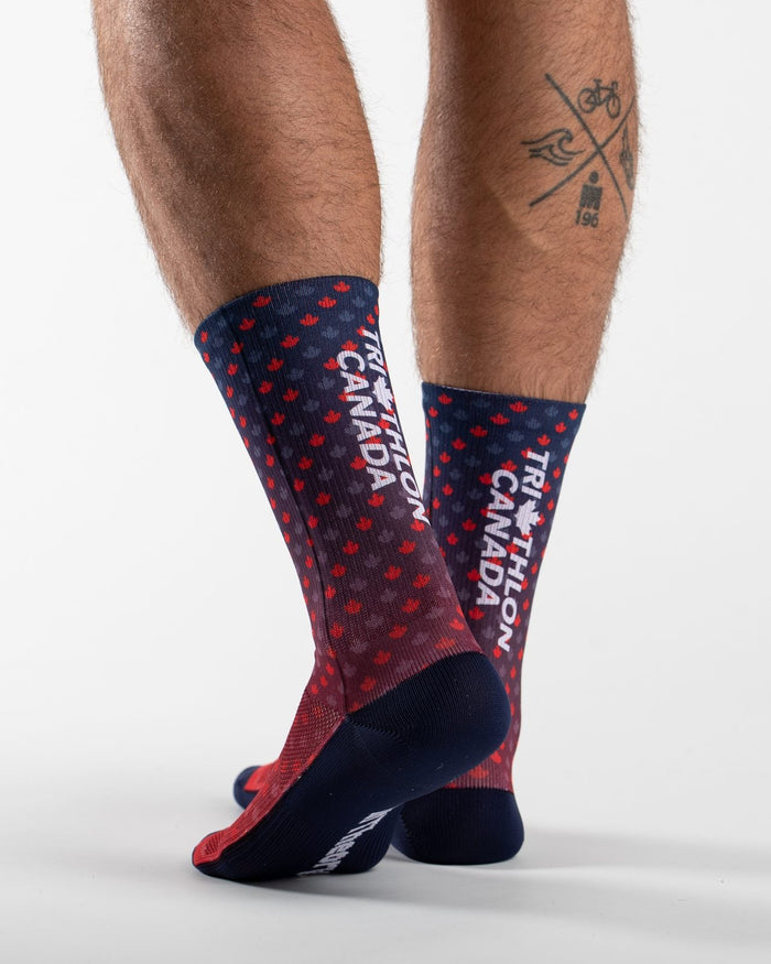 A pair of crew socks worn, shown from the side against a clean white studio background. The socks are navy blue with red maple leafs and white text reading 'TRIATHLON CANADA'.